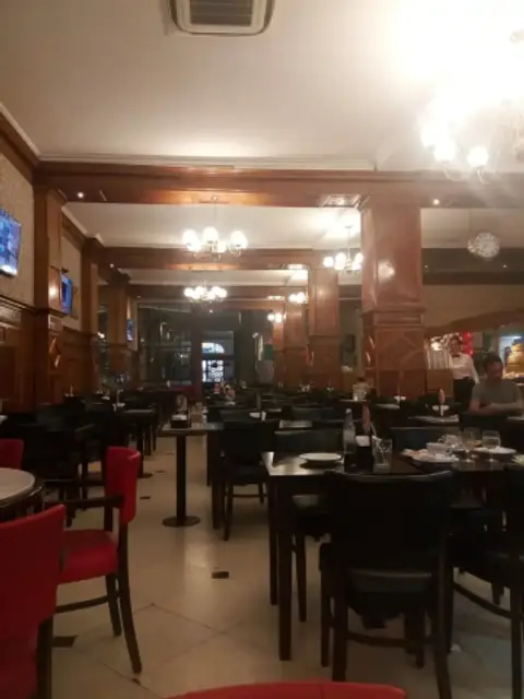 Panelled café room with chandeliers, dark wood piers and tables laid with white cups