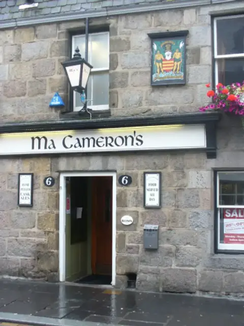 Grey granite frontage with a white lettered fascia, a lantern and the burgh arms above the door