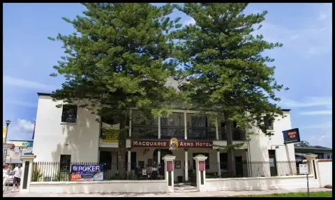 White rendered two-storey hotel with a colonnaded verandah and lettered sign, behind two pines