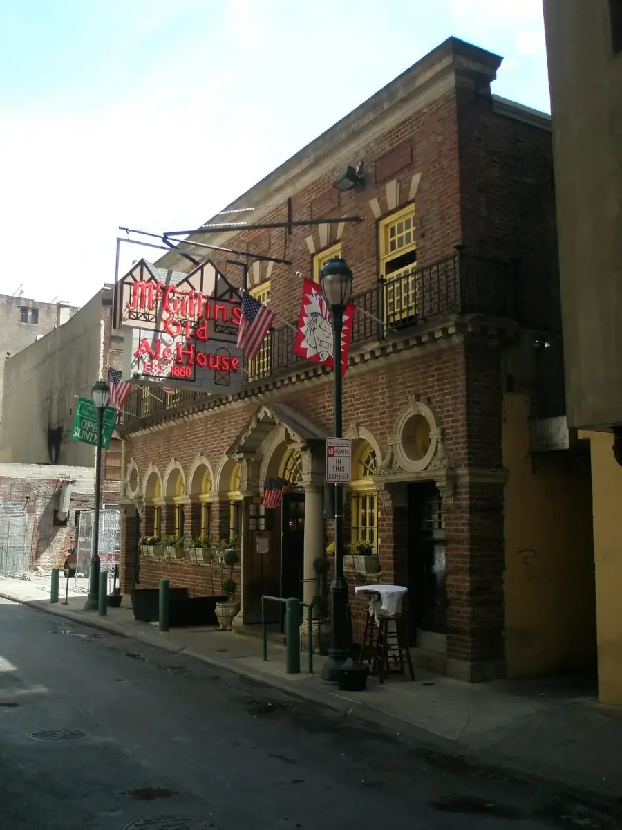 Red-brick building with arcaded ground floor, iron balcony and a red neon sign on a narrow street