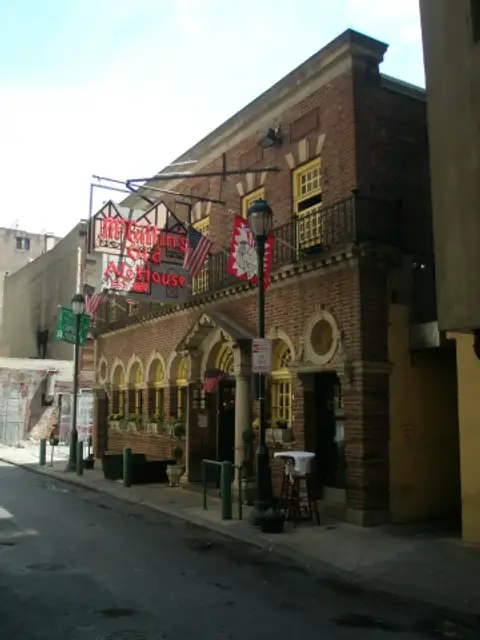 Red-brick building with arcaded ground floor, iron balcony and a red neon sign on a narrow street