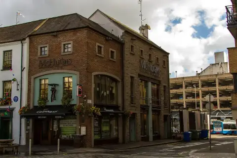 Brick and stone corner bar of three storeys with green-painted shopfronts and hanging baskets