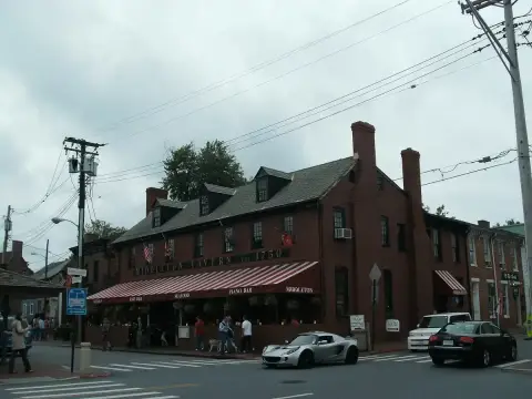 Dark red brick tavern with dormer windows, tall chimneys and a striped awning over the pavement
