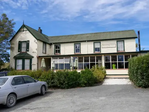 Cream weatherboard inn with a green corrugated roof and a long glazed verandah bar