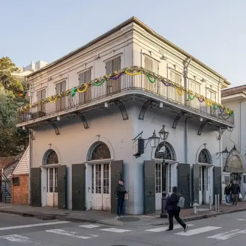 Cream stuccoed corner building with an iron balcony hung with garlands and shuttered arched doors