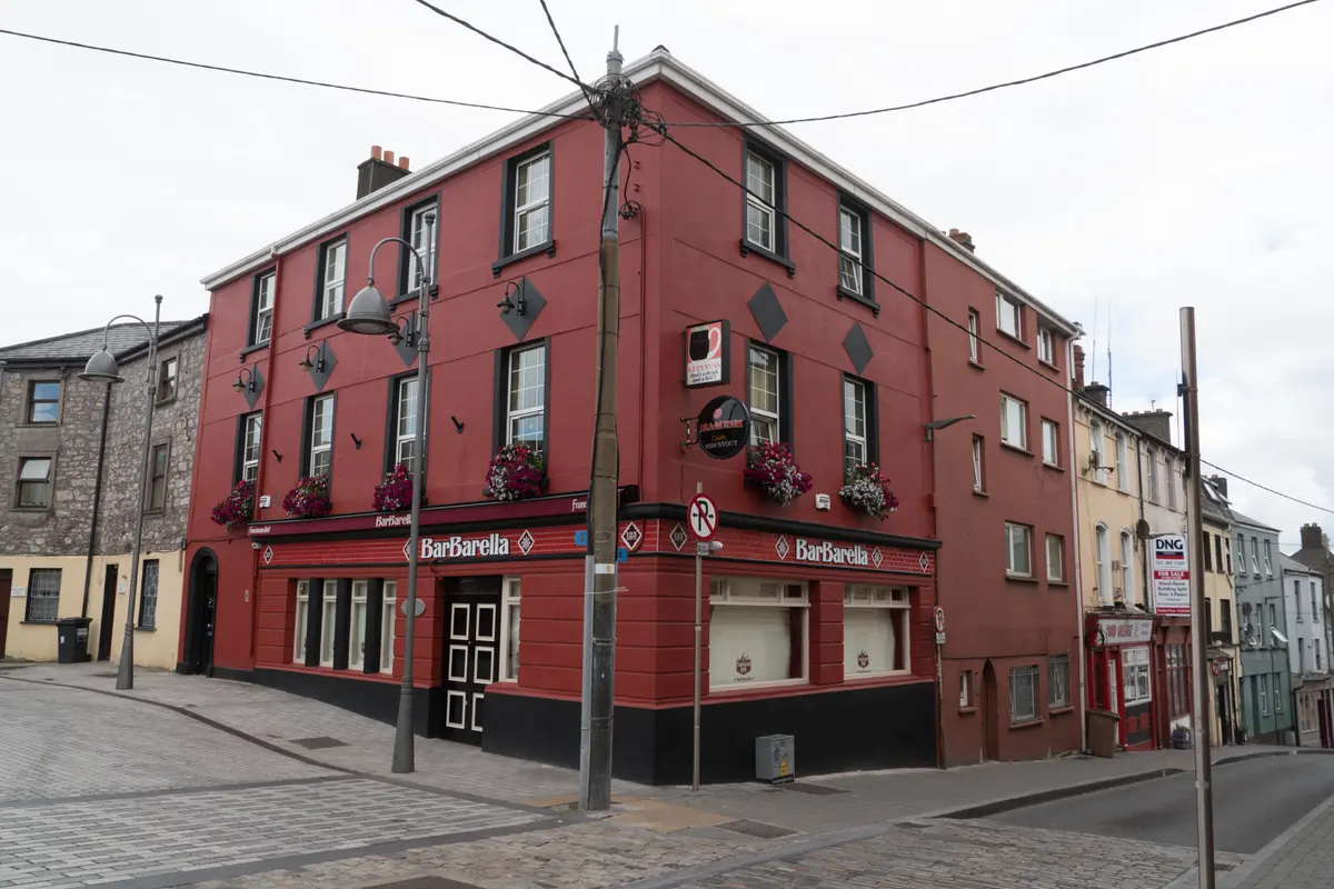 Red-painted three-storey corner pub on Barrack Street, Cork, trading as BarBarella, with diamond plaques and window boxes