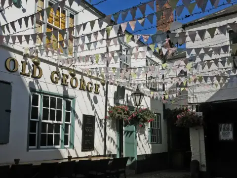 White courtyard walls with large gold lettering, hanging baskets and bunting strung overhead