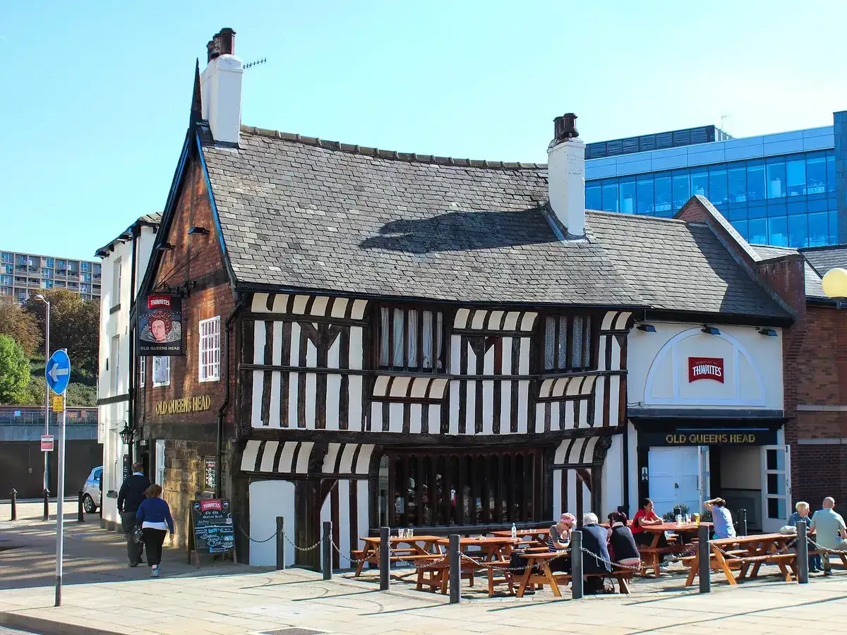 Timber-framed house with close-set studding and a heavy stone-slate roof, tables outside