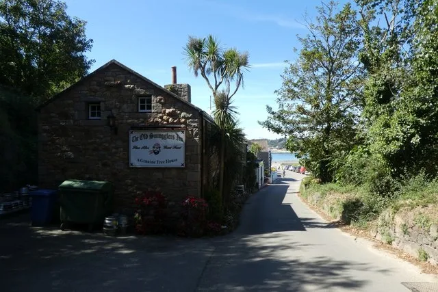 Granite gable end with the inn's painted free-house sign, beside a lane running down to Ouaisné Bay
