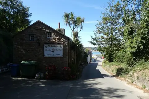 Granite gable end with the inn's painted free-house sign, beside a lane running down to Ouaisné Bay