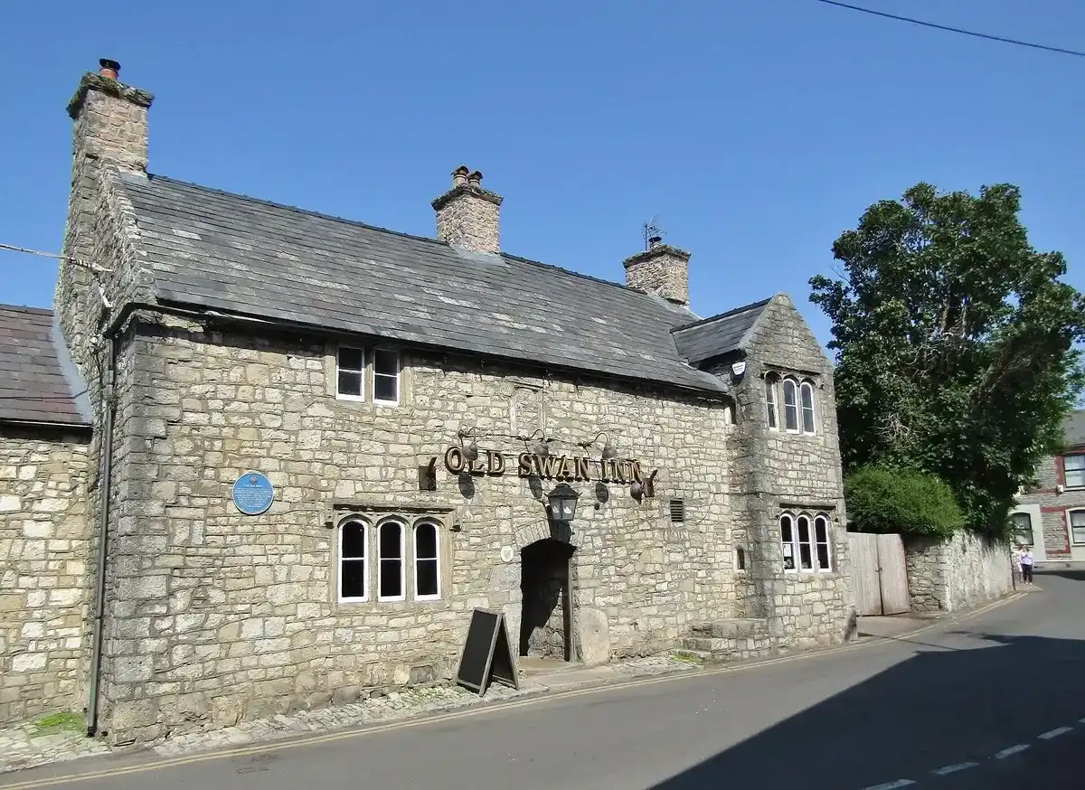 Stone inn with OLD SWAN INN in gold letters across the front, a gabled wing and tall chimneys