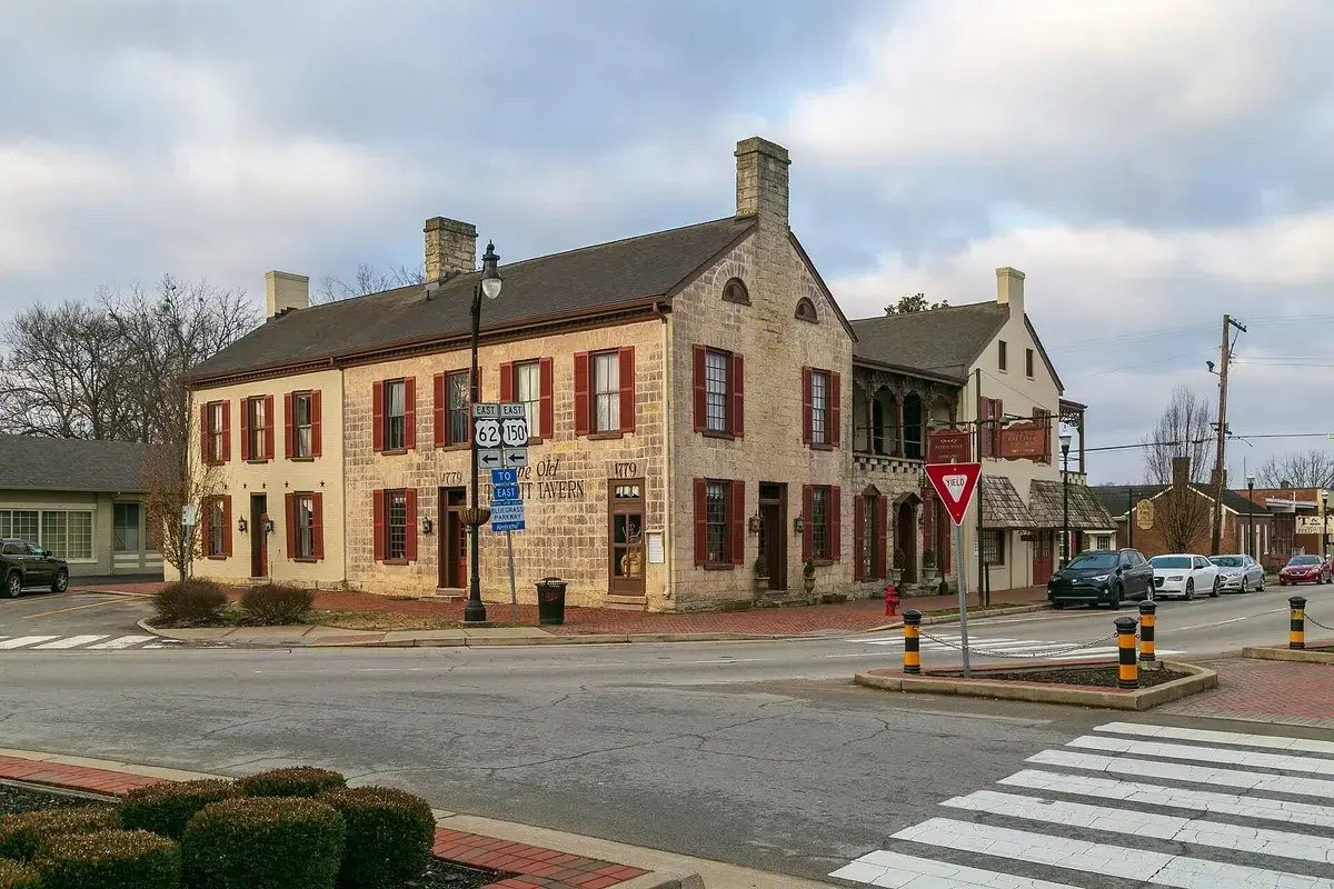 Two-storey limestone tavern with red shutters and stone chimneys on a town crossroads