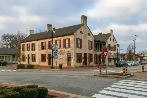 Two-storey limestone tavern with red shutters and stone chimneys on a town crossroads