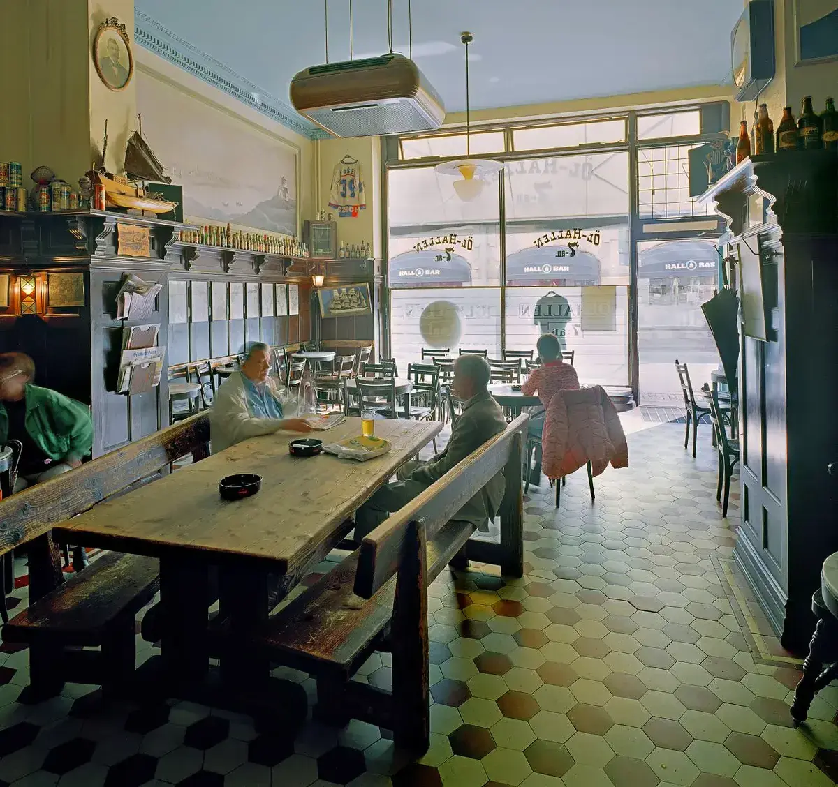 Beer hall with long scrubbed tables and benches; the window reads Öl-hallen 7:an in reverse