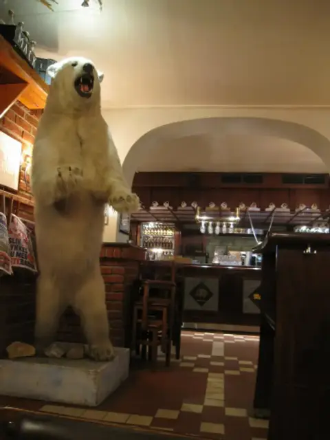 Stuffed polar bear on a plinth beside the bar, with a tiled floor and glasses racked behind