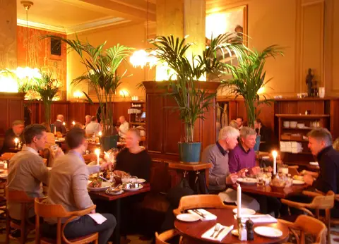 Beer hall with wood panelling, tall palms in pots, globe lamps and a candle on every table