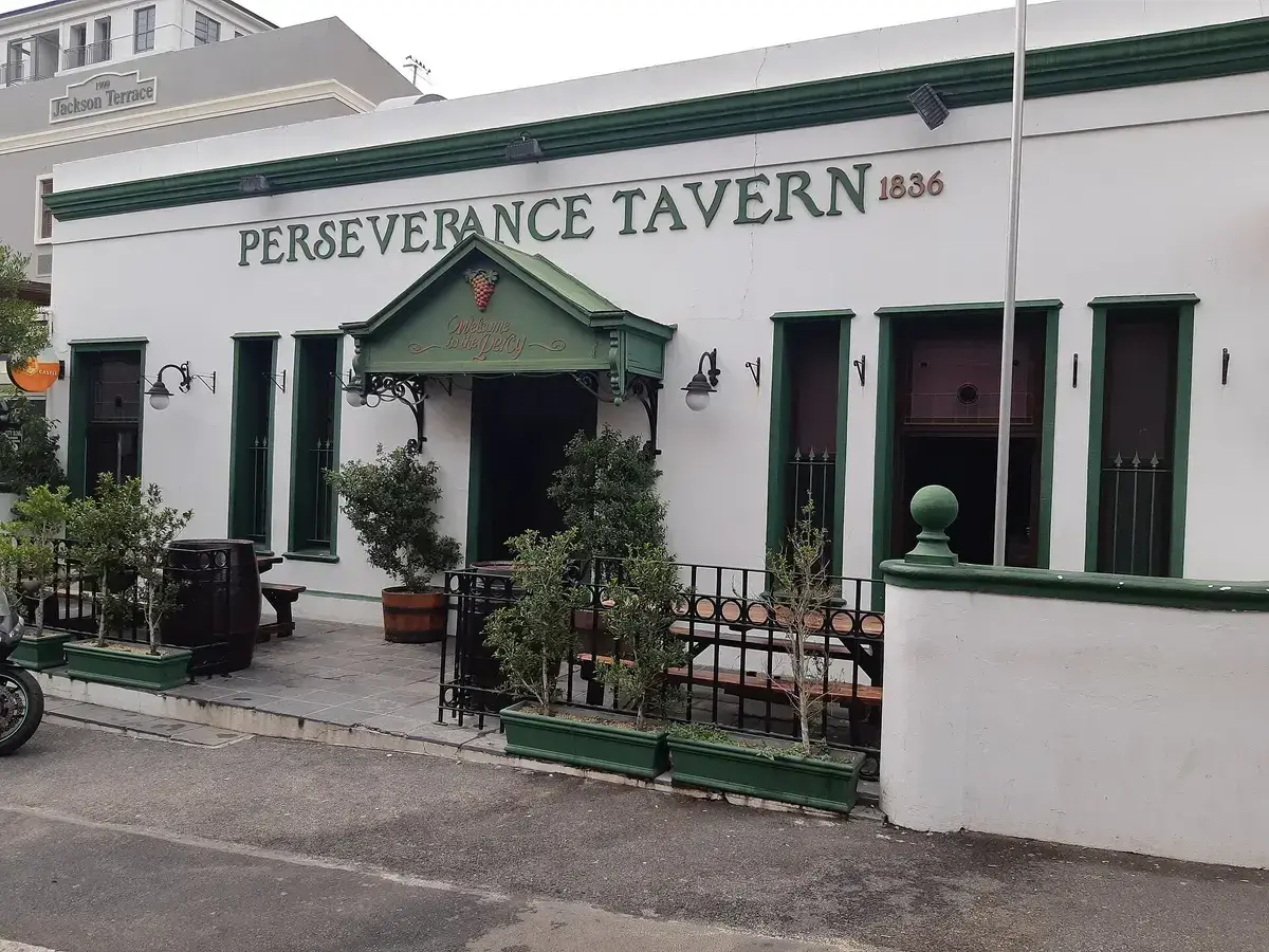 White single-storey tavern with dark green joinery, a small pedimented porch and bay trees