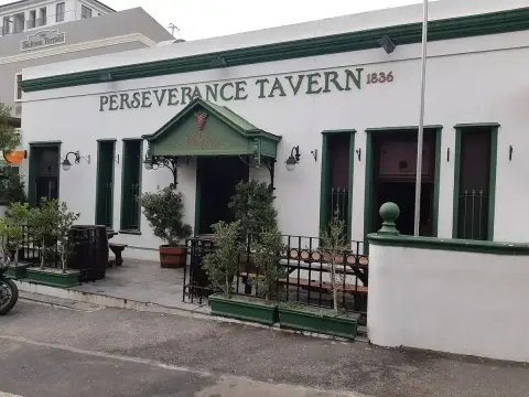 White single-storey tavern with dark green joinery, a small pedimented porch and bay trees