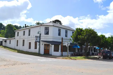 White two-storey inn on a corner with a corrugated roof, stoep and a Pig n Whistle Hotel sign