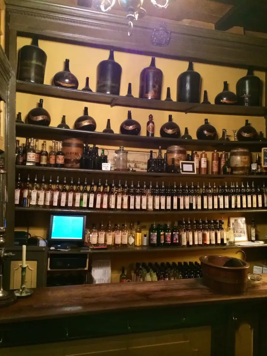 Wooden shelves behind a bar filled with rows of labelled liqueur bottles and old stoneware jars