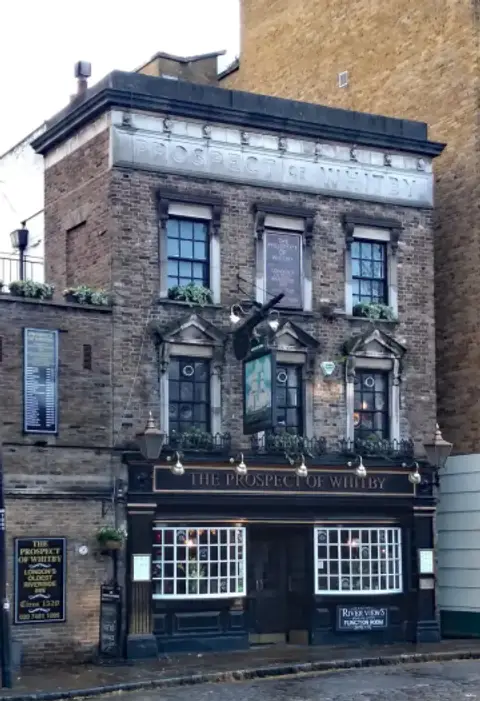 Three-storey brick pub with a stone name band, pedimented windows and a black lettered fascia