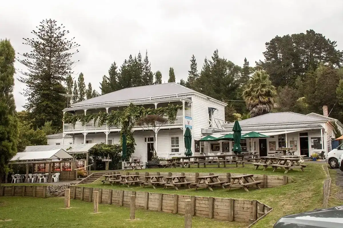 Two-storey white weatherboard hotel with a vine-covered veranda, picnic tables on the grass below