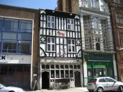 Narrow timber-framed pub wedged between a brick warehouse and a curry house, red lion carved above the windows