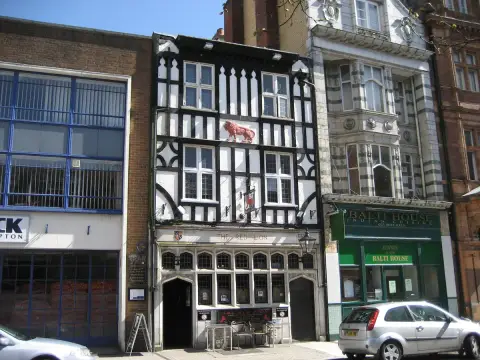 Narrow timber-framed pub wedged between a brick warehouse and a curry house, red lion carved above the windows