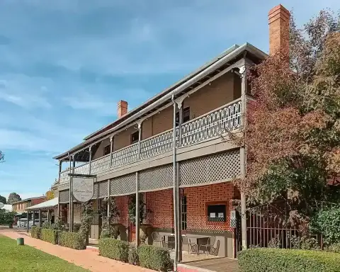 Two-storey brick hotel with a lace-ironwork verandah and lattice screens, along a footpath
