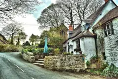 Whitewashed inn beside a stone church tower, parasol and benches on the terrace above the lane