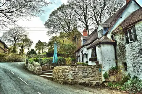 Whitewashed inn beside a stone church tower, parasol and benches on the terrace above the lane