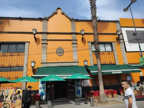Orange rendered building with a scrolled parapet, green awnings and mariachi murals alongside