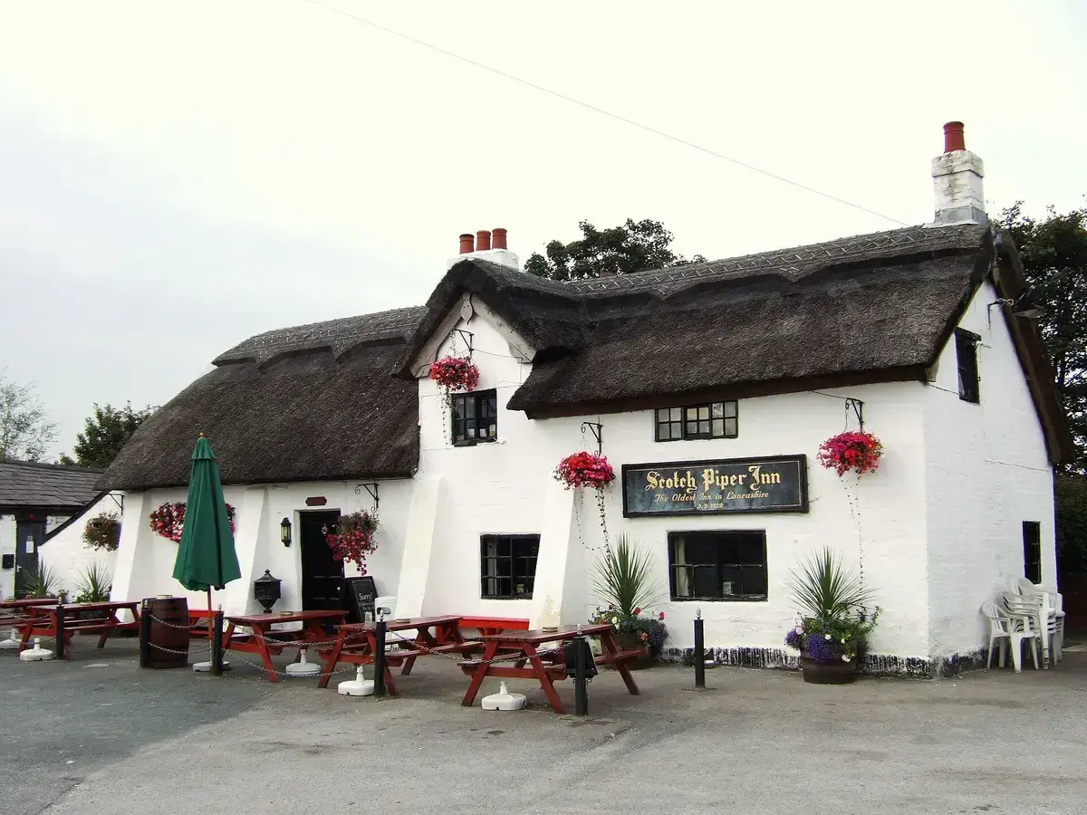 Thatched, whitewashed inn with three brick chimneys, a gold-lettered board and picnic tables