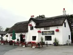 Thatched, whitewashed inn with three brick chimneys, a gold-lettered board and picnic tables