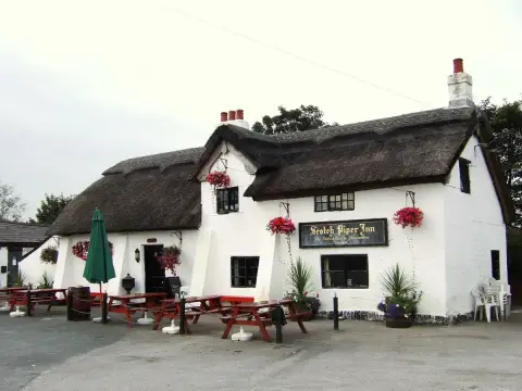 Thatched, whitewashed inn with three brick chimneys, a gold-lettered board and picnic tables