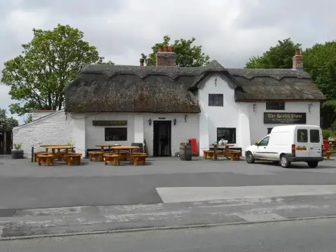 Long thatched, whitewashed inn with brick chimneys and benches on the forecourt by the road