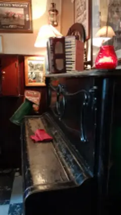 Worn black wooden bar counter under lamplight, with an accordion, old framed adverts and a lantern