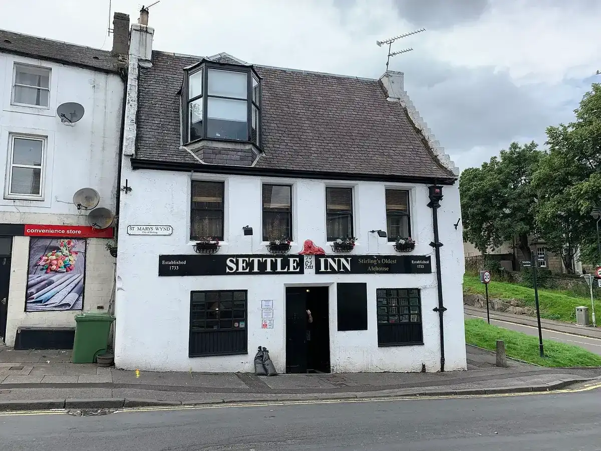 White harled inn with a pantiled roof, dormer and black fascia lettered Settle Inn, on a wynd