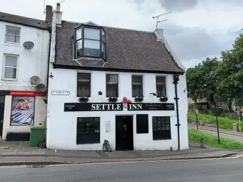 White harled inn with a pantiled roof, dormer and black fascia lettered Settle Inn, on a wynd