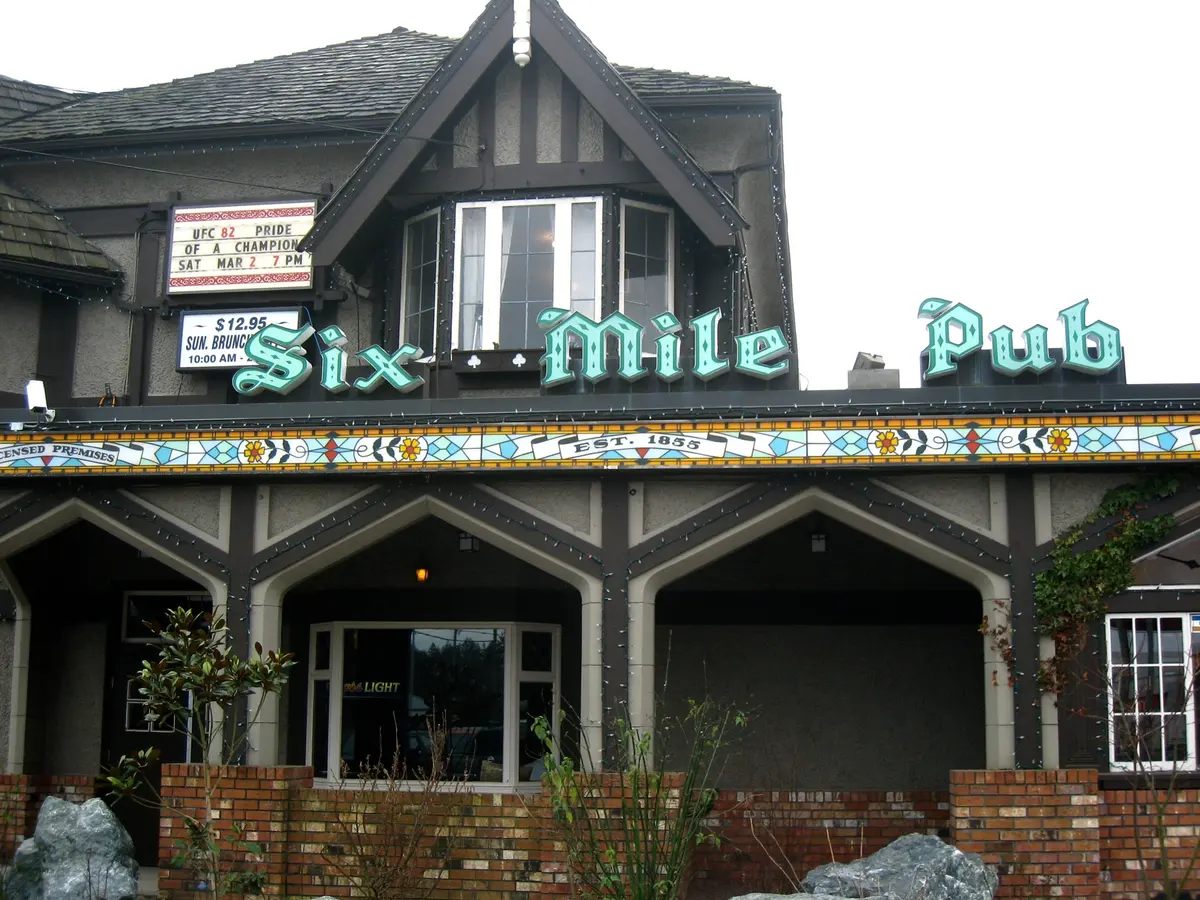 Front of the Six Mile Pub: green lettering over a stained-glass fascia reading Est. 1855, a half-timbered dormer and arched porch bays