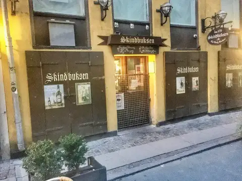 Ochre frontage with brown shutters lettered Skindbuksen, old Tuborg posters and a hanging sign