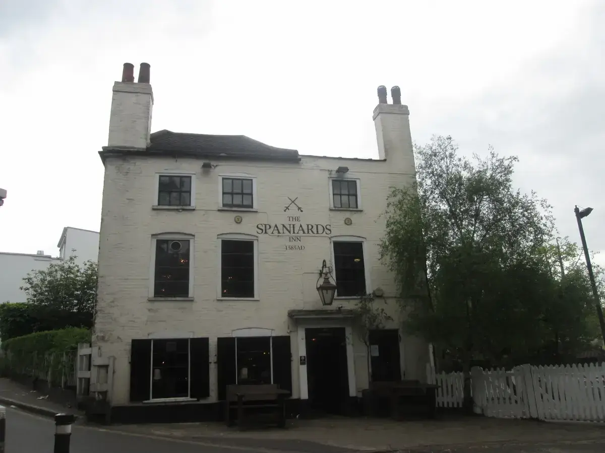 Cream-painted brick inn with two tall chimneys and a lamp over the door, benches outside