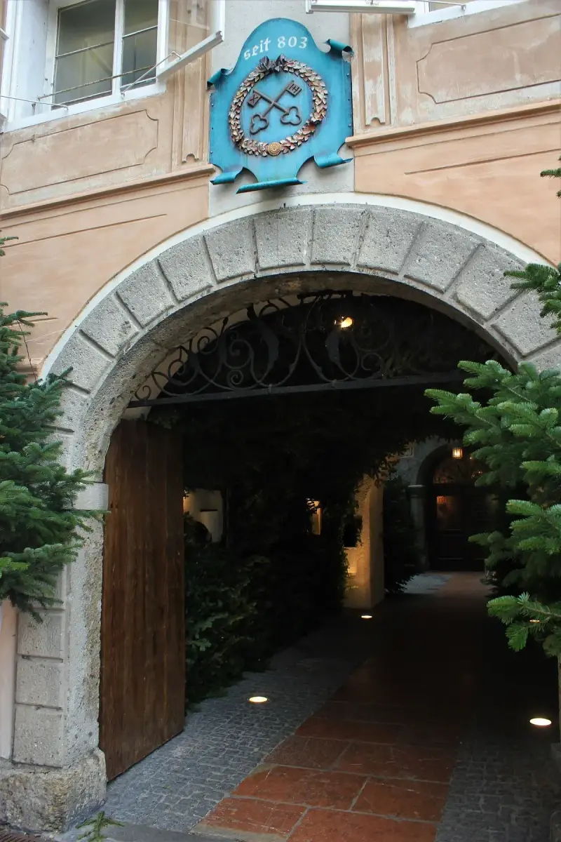 Stone archway into a courtyard, a blue shield above it with crossed keys and the words seit 803