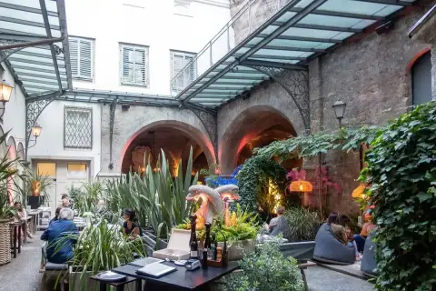 Glass-roofed courtyard with tables and chairs, stone arcades down one side and ivy above