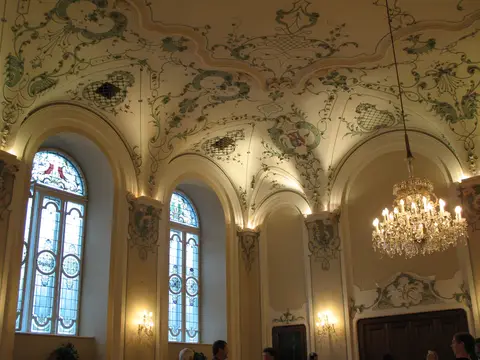 Painted and moulded baroque vault with tall stained-glass windows below and a crystal chandelier