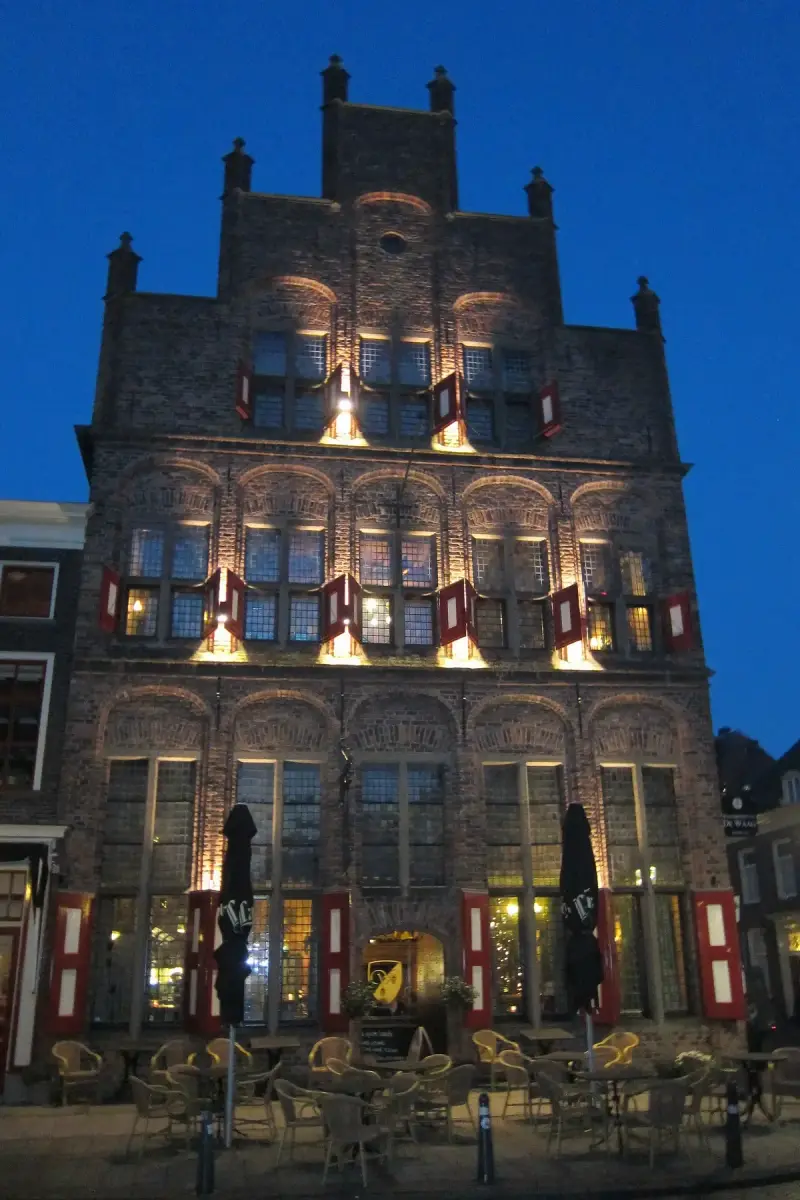 The same brick gable lit from below at dusk against a deep blue sky, cafe chairs empty in front