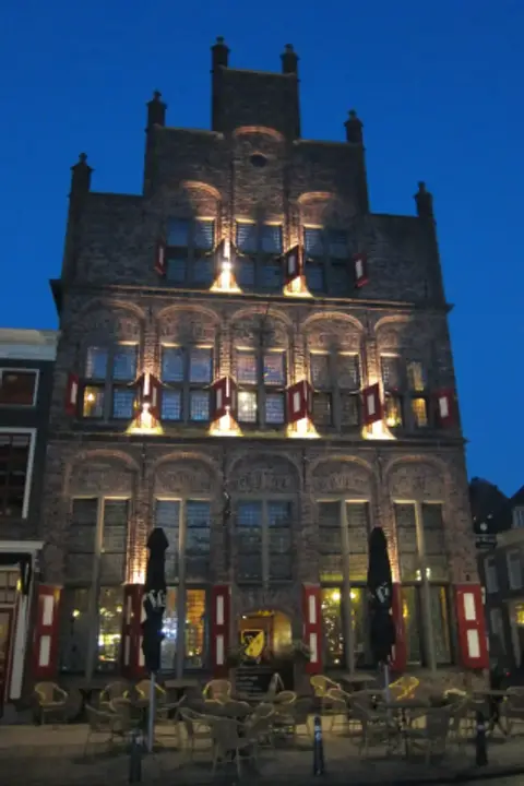 The same brick gable lit from below at dusk against a deep blue sky, cafe chairs empty in front