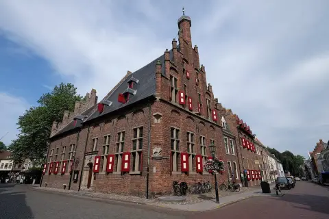 Tall brick stepped-gable hall with red and white shutters on a cobbled corner, bicycles against the wall