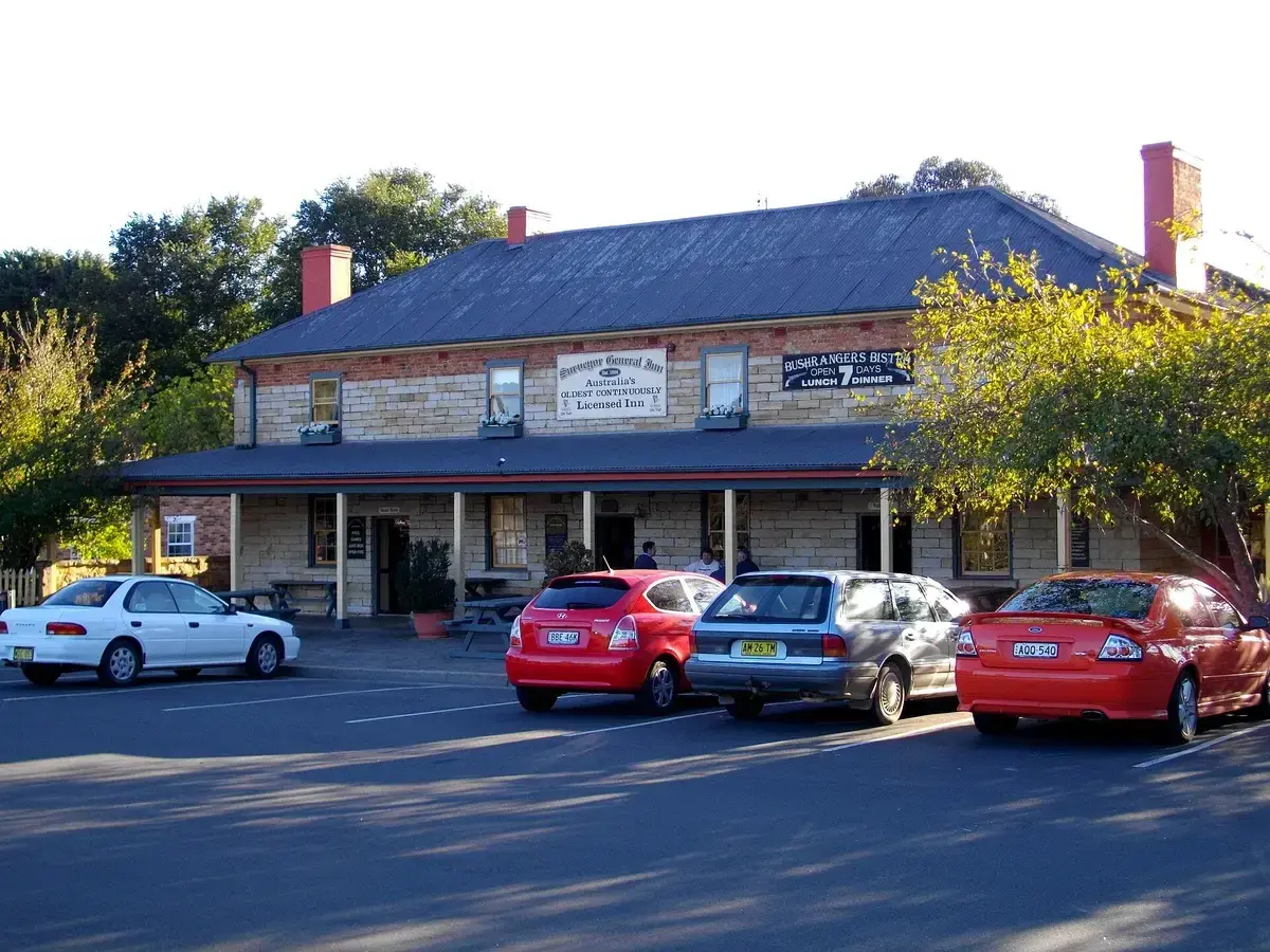 Two-storey sandstone inn with a verandah along the front and a painted sign between windows