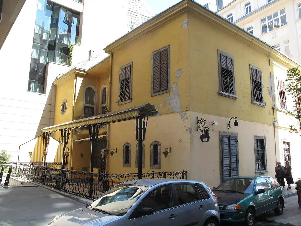 Corner of a yellow baroque palace, a striped awning over the restaurant terrace and an iron sign bracket